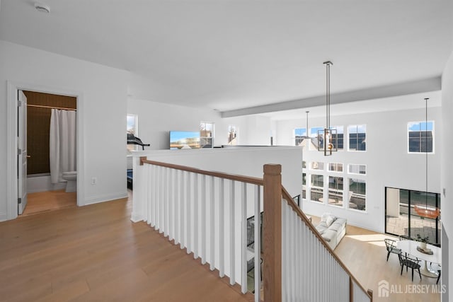 hall with baseboards, an upstairs landing, an inviting chandelier, and wood finished floors