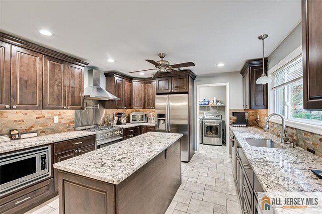 kitchen featuring decorative light fixtures, tasteful backsplash, sink, stainless steel appliances, and wall chimney exhaust hood