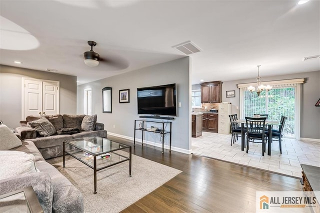 living room with ceiling fan with notable chandelier and light hardwood / wood-style floors