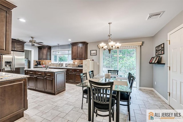 kitchen featuring pendant lighting, stainless steel refrigerator with ice dispenser, dark brown cabinetry, a kitchen island, and ceiling fan with notable chandelier