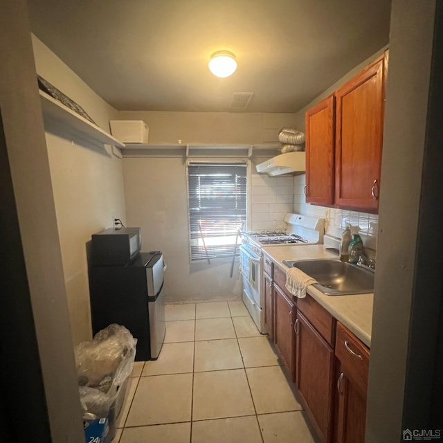 kitchen featuring white range with gas cooktop, sink, backsplash, light tile patterned flooring, and wall chimney exhaust hood