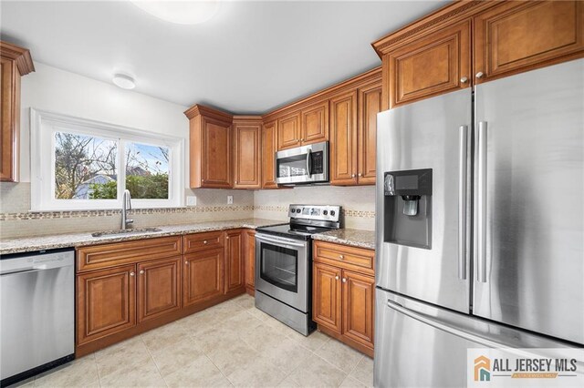 kitchen with light stone countertops, appliances with stainless steel finishes, decorative backsplash, and sink