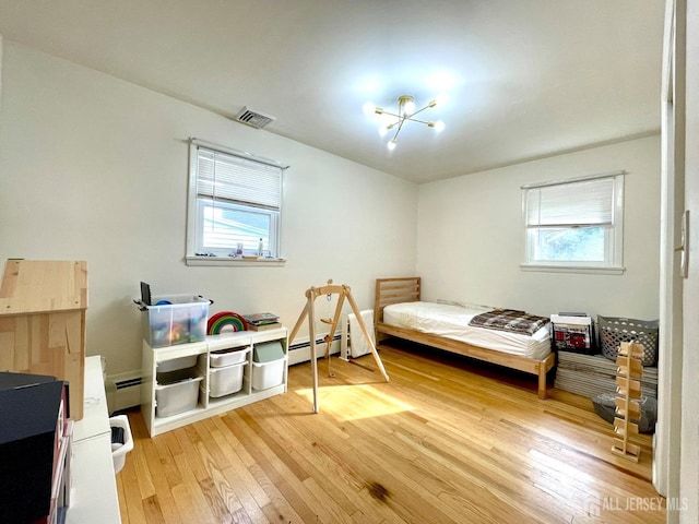 bedroom featuring hardwood / wood-style flooring, an inviting chandelier, multiple windows, and baseboard heating