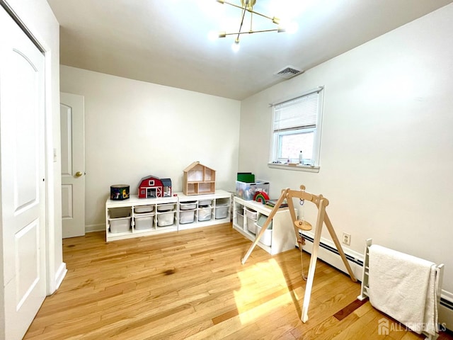 rec room featuring hardwood / wood-style floors, a notable chandelier, and a baseboard heating unit