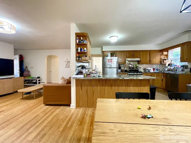 kitchen featuring light wood-type flooring, appliances with stainless steel finishes, a kitchen breakfast bar, kitchen peninsula, and dark stone counters