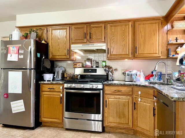 kitchen featuring sink, tasteful backsplash, dark stone counters, light tile patterned floors, and appliances with stainless steel finishes