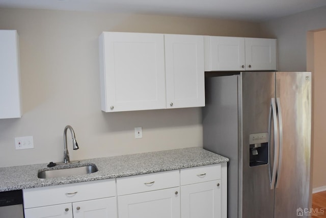 kitchen featuring light stone countertops, stainless steel fridge, white cabinetry, and sink