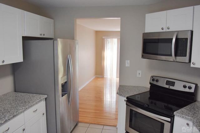 kitchen with light tile patterned floors, light stone countertops, white cabinetry, and appliances with stainless steel finishes