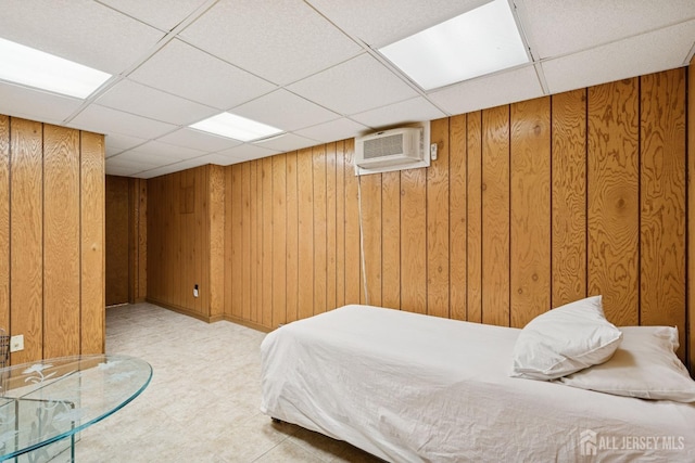 bedroom with a paneled ceiling, wood walls, a wall unit AC, and light floors