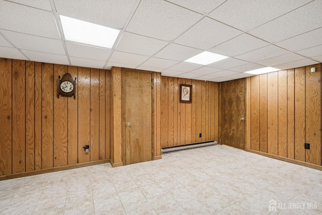 finished below grade area with a drop ceiling, baseboard heating, and wood walls