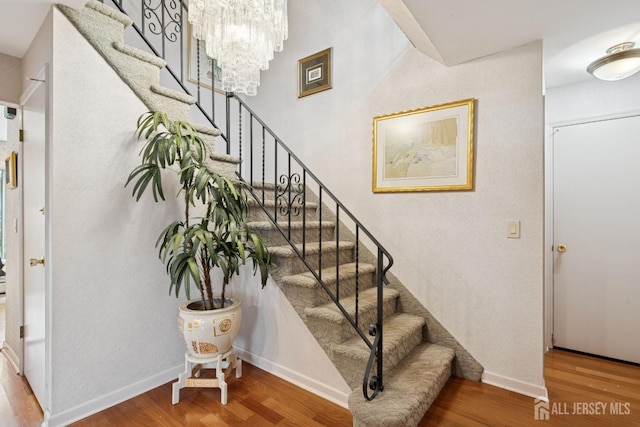 stairs featuring baseboards, a chandelier, and wood finished floors