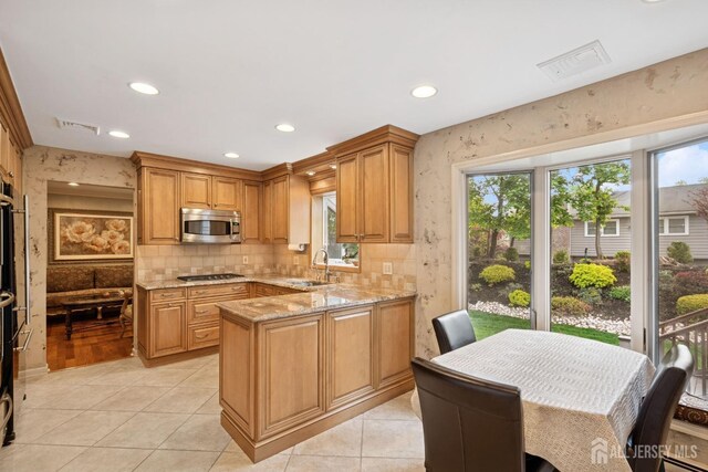 kitchen with light stone counters, visible vents, a sink, a peninsula, and appliances with stainless steel finishes