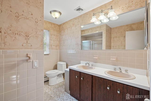 bathroom featuring toilet, tile walls, wallpapered walls, and a sink