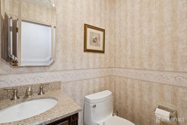 half bathroom with wallpapered walls, toilet, and vanity