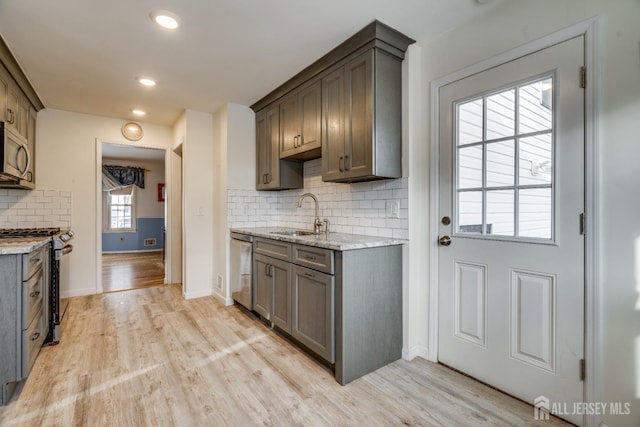 kitchen featuring sink, light wood-type flooring, appliances with stainless steel finishes, light stone countertops, and backsplash