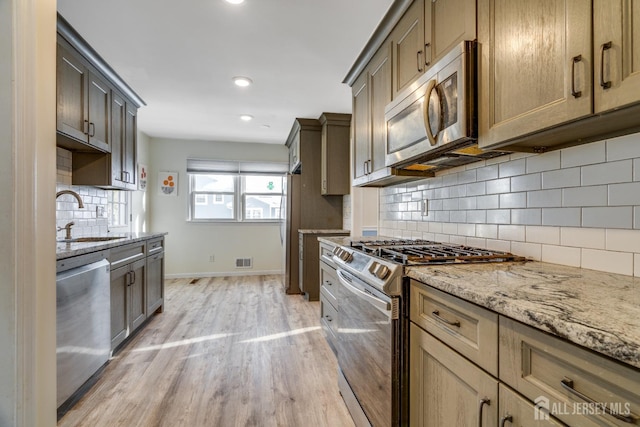 kitchen featuring sink, light stone counters, light hardwood / wood-style flooring, stainless steel appliances, and backsplash