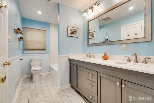 full bathroom featuring vanity, tiled shower / bath, and toilet