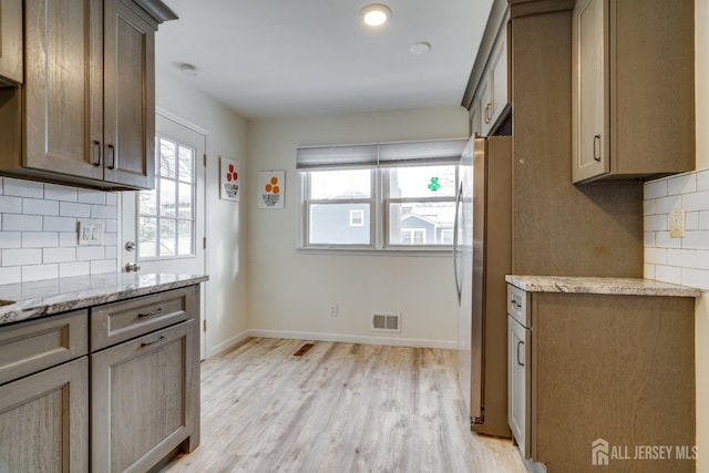 kitchen with light stone counters, decorative backsplash, light hardwood / wood-style flooring, and stainless steel refrigerator