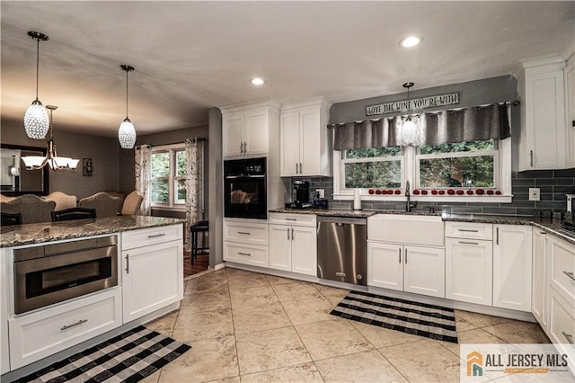 kitchen with pendant lighting, sink, appliances with stainless steel finishes, dark stone countertops, and white cabinets