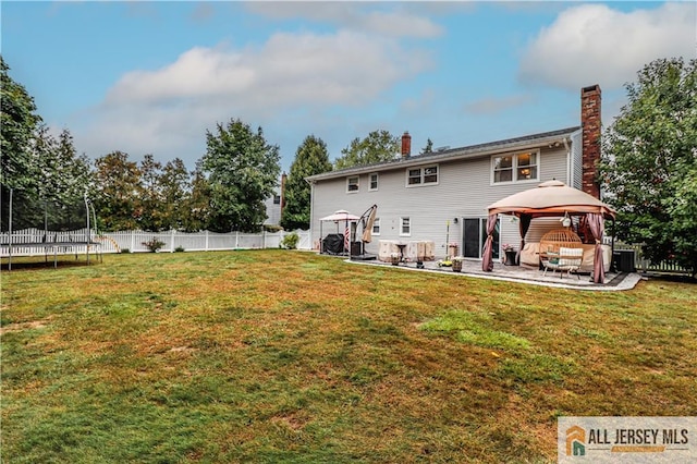 rear view of property with a gazebo, a patio, a trampoline, and a lawn