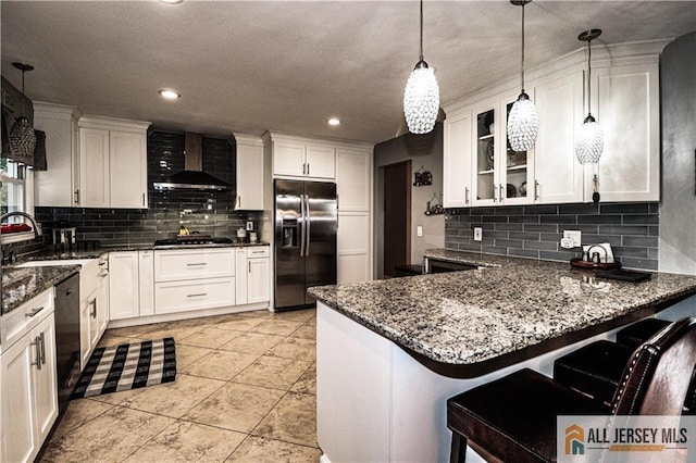 kitchen featuring appliances with stainless steel finishes, decorative light fixtures, white cabinetry, a kitchen breakfast bar, and wall chimney range hood