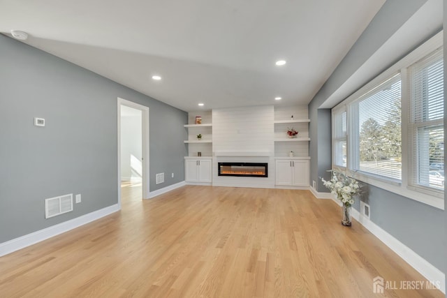 unfurnished living room featuring light wood finished floors, recessed lighting, visible vents, a glass covered fireplace, and baseboards