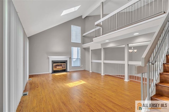 22 Witch Hazel Ct, South Brunswick, NJ 08852 - unfurnished living room featuring high vaulted ceiling, a fireplace with flush hearth, a skylight, stairway, and wood finished floors