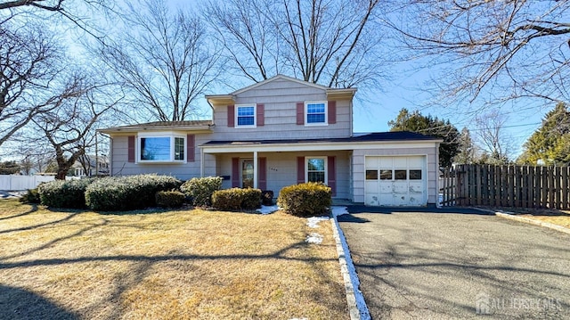 tri-level home with a garage, a front lawn, fence, and aphalt driveway