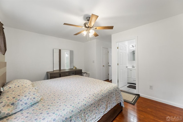 bedroom featuring ceiling fan, a sink, wood finished floors, baseboards, and ensuite bath