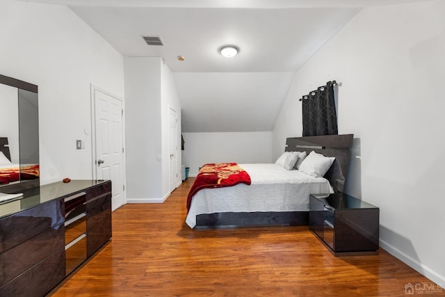 bedroom featuring vaulted ceiling, wood finished floors, visible vents, and baseboards