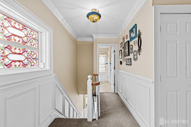 hallway with an upstairs landing, a decorative wall, crown molding, a wainscoted wall, and light carpet
