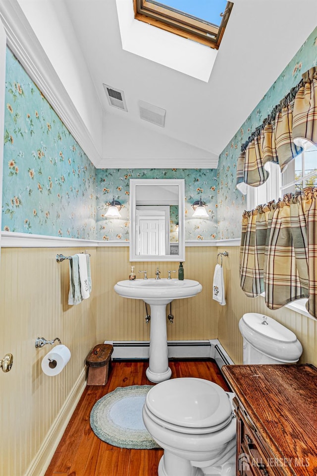 bathroom with a wainscoted wall, toilet, wallpapered walls, wood finished floors, and a skylight