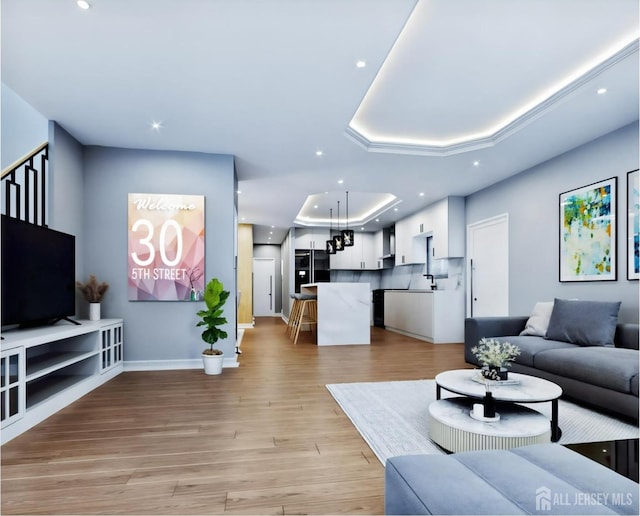 living room with a tray ceiling, light wood-style flooring, baseboards, and recessed lighting