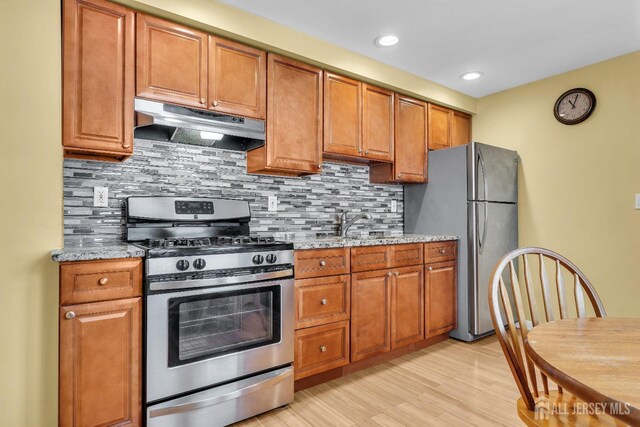 kitchen featuring sink, light stone counters, tasteful backsplash, stainless steel appliances, and light hardwood / wood-style floors