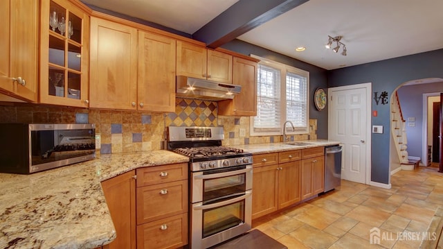 kitchen featuring appliances with stainless steel finishes, beamed ceiling, sink, decorative backsplash, and light stone countertops