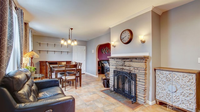 living room featuring crown molding, a stone fireplace, and a notable chandelier