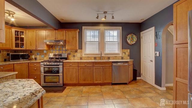 kitchen featuring appliances with stainless steel finishes, light stone countertops, sink, and backsplash