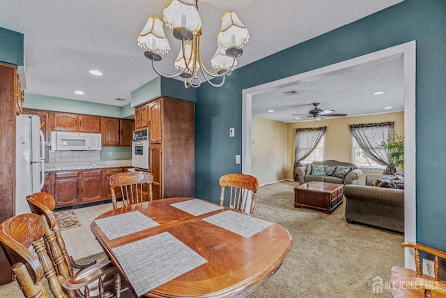 dining room with ceiling fan with notable chandelier, a textured ceiling, and light carpet