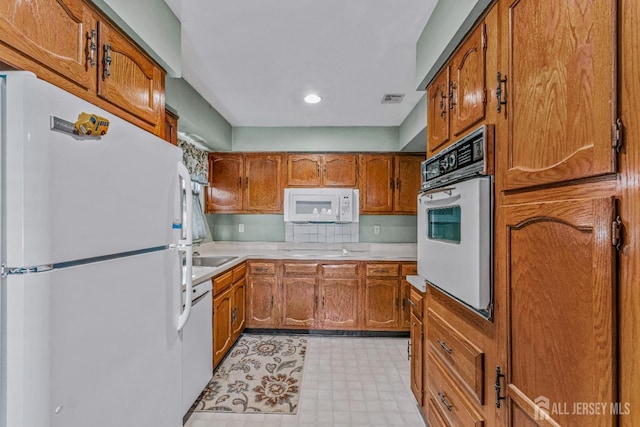 kitchen with light floors, light countertops, visible vents, brown cabinetry, and white appliances