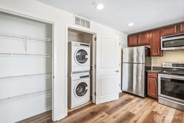 kitchen featuring visible vents, stacked washing maching and dryer, stainless steel appliances, decorative backsplash, and light wood-type flooring