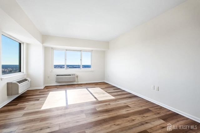 spare room with an AC wall unit, wood finished floors, baseboards, and a wall mounted air conditioner