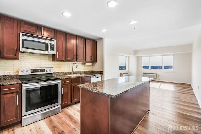 kitchen featuring a sink, decorative backsplash, an AC wall unit, light wood-style floors, and appliances with stainless steel finishes