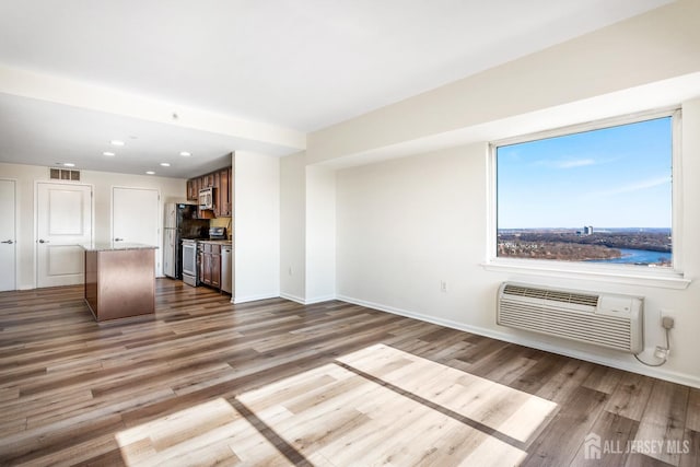 unfurnished living room with visible vents, a wall mounted air conditioner, baseboards, and wood finished floors