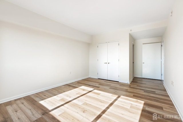 unfurnished bedroom with a closet, baseboards, and light wood finished floors