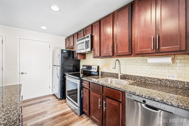 kitchen with light wood-style flooring, a sink, reddish brown cabinets, appliances with stainless steel finishes, and decorative backsplash