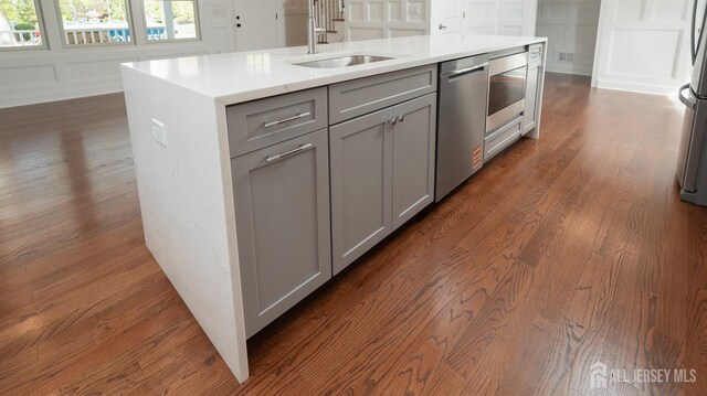 kitchen with gray cabinets, a sink, dark wood-style flooring, stainless steel appliances, and a decorative wall