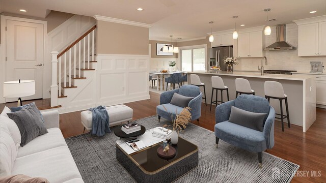 living room with wood finished floors, ornamental molding, stairway, recessed lighting, and a decorative wall