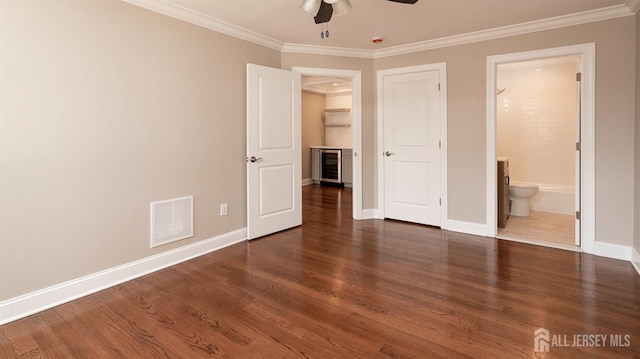 unfurnished bedroom with beverage cooler, crown molding, baseboards, wood finished floors, and connected bathroom