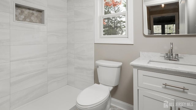 bathroom featuring toilet, vanity, a tile shower, and baseboards