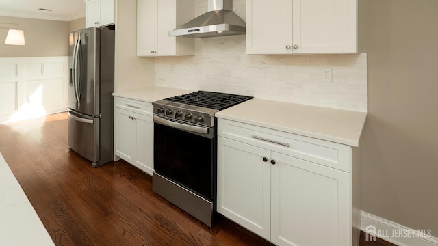 kitchen featuring appliances with stainless steel finishes, wall chimney exhaust hood, ornamental molding, white cabinetry, and dark wood-style floors